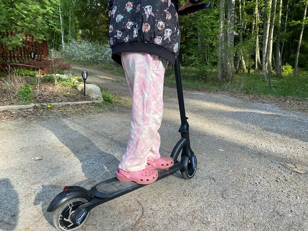 Ett barn kör en elsparkcykel konstruerad för barn, på en grusväg